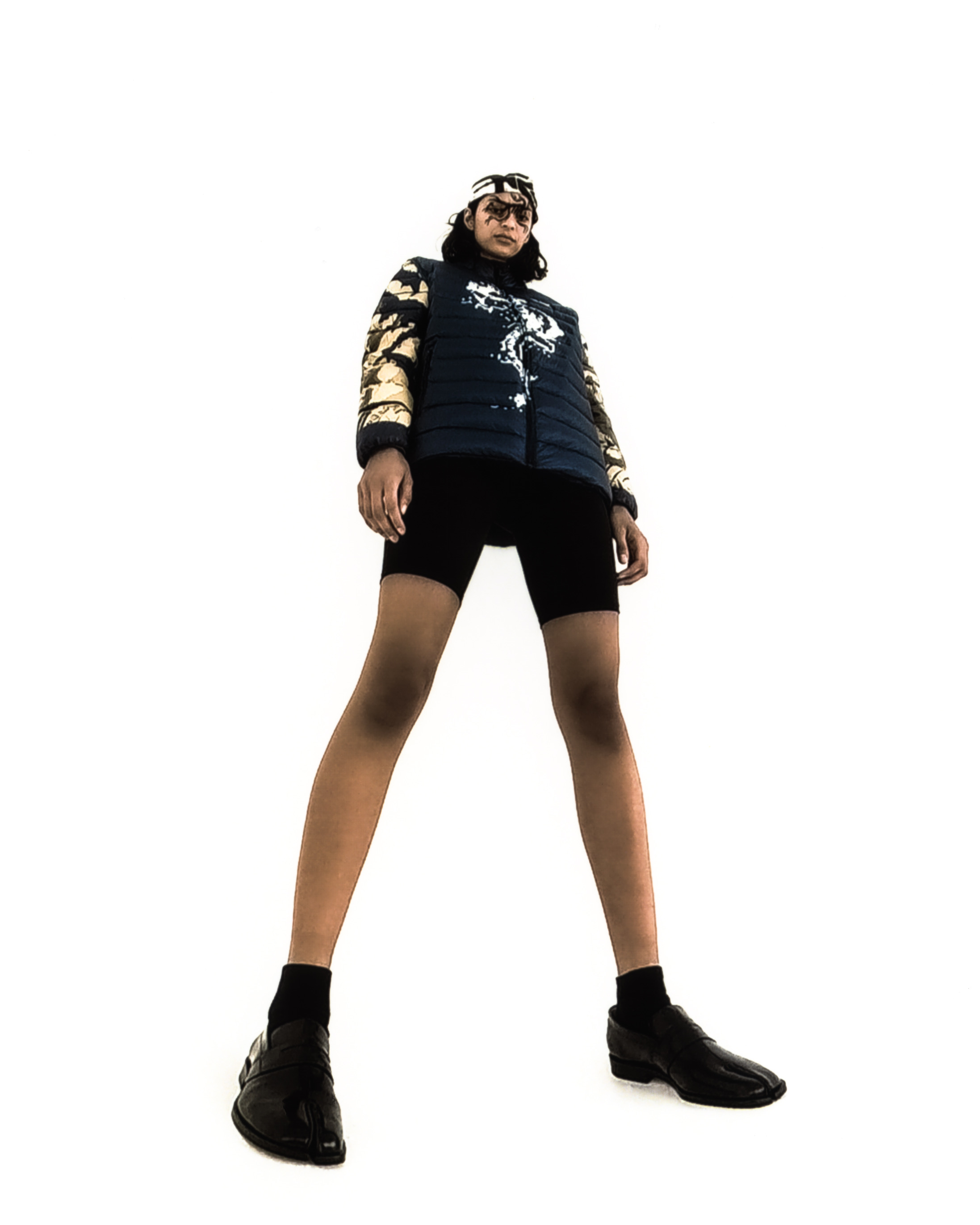 Full body shot of a model wearing glack graphic liner, a puffer vest and bandana against a white background